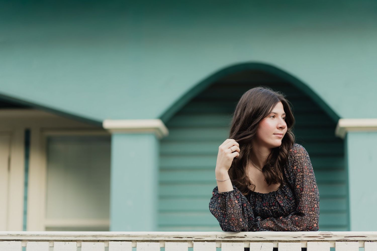 Woman in dark knit sweater stands against a teal wall in a lifestyle portrait series.