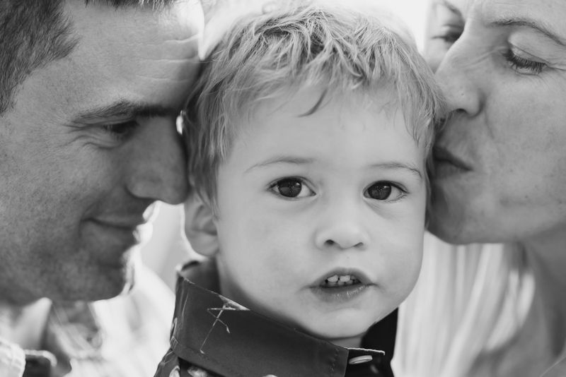 A series of black and white photos showing tender moments between parents and a small child with kisses and smiles.