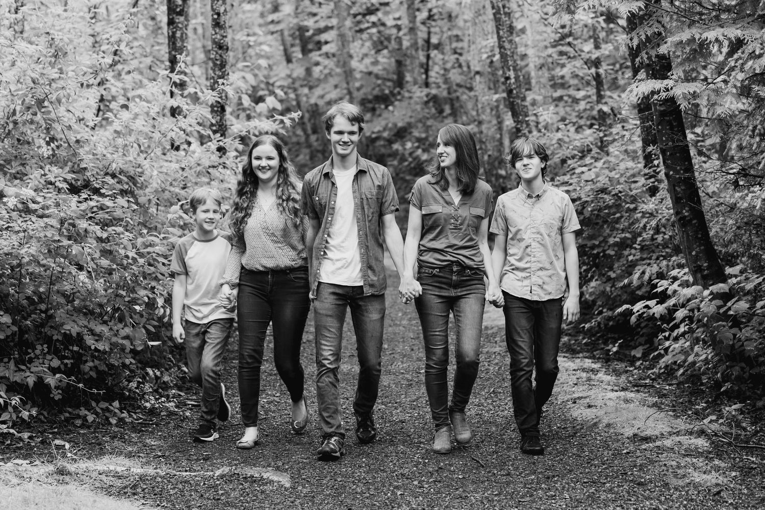 A group walks together on a wooded path wearing casual clothing in black and white tones.