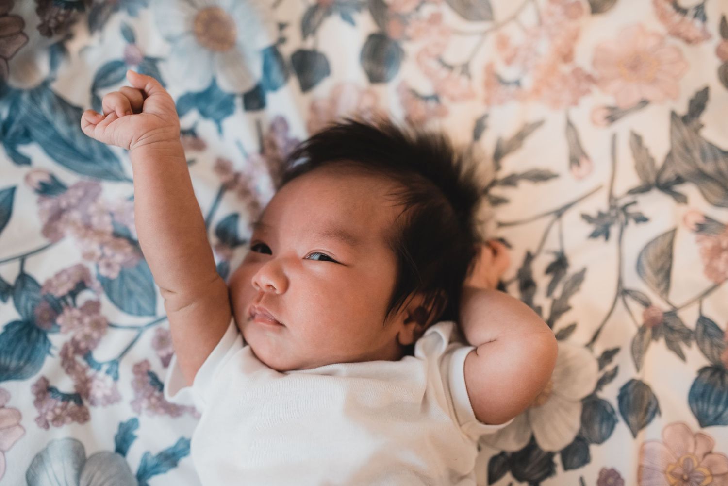 Baby lying on floral patterned fabric with arms stretched overhead.