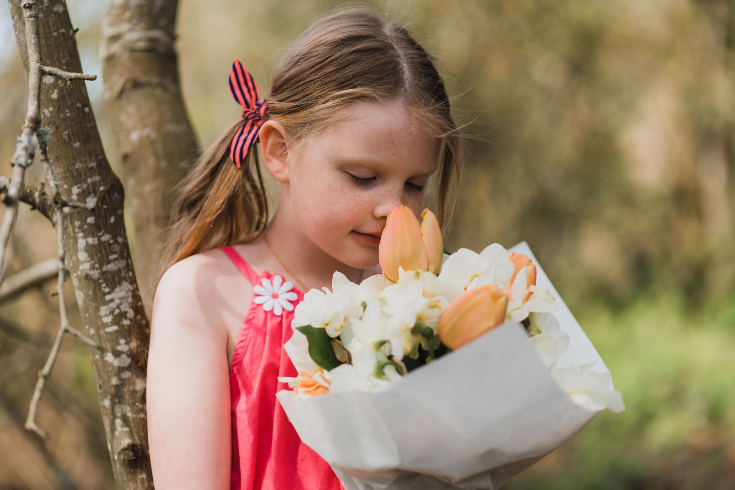 Two people sharing a tender moment while holding a bouquet of white and peach flowers near a birch tree.