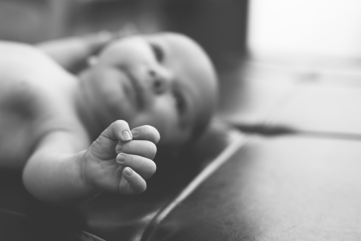 Close-up black and white photo of tiny baby fingers grasping gently against a soft background.