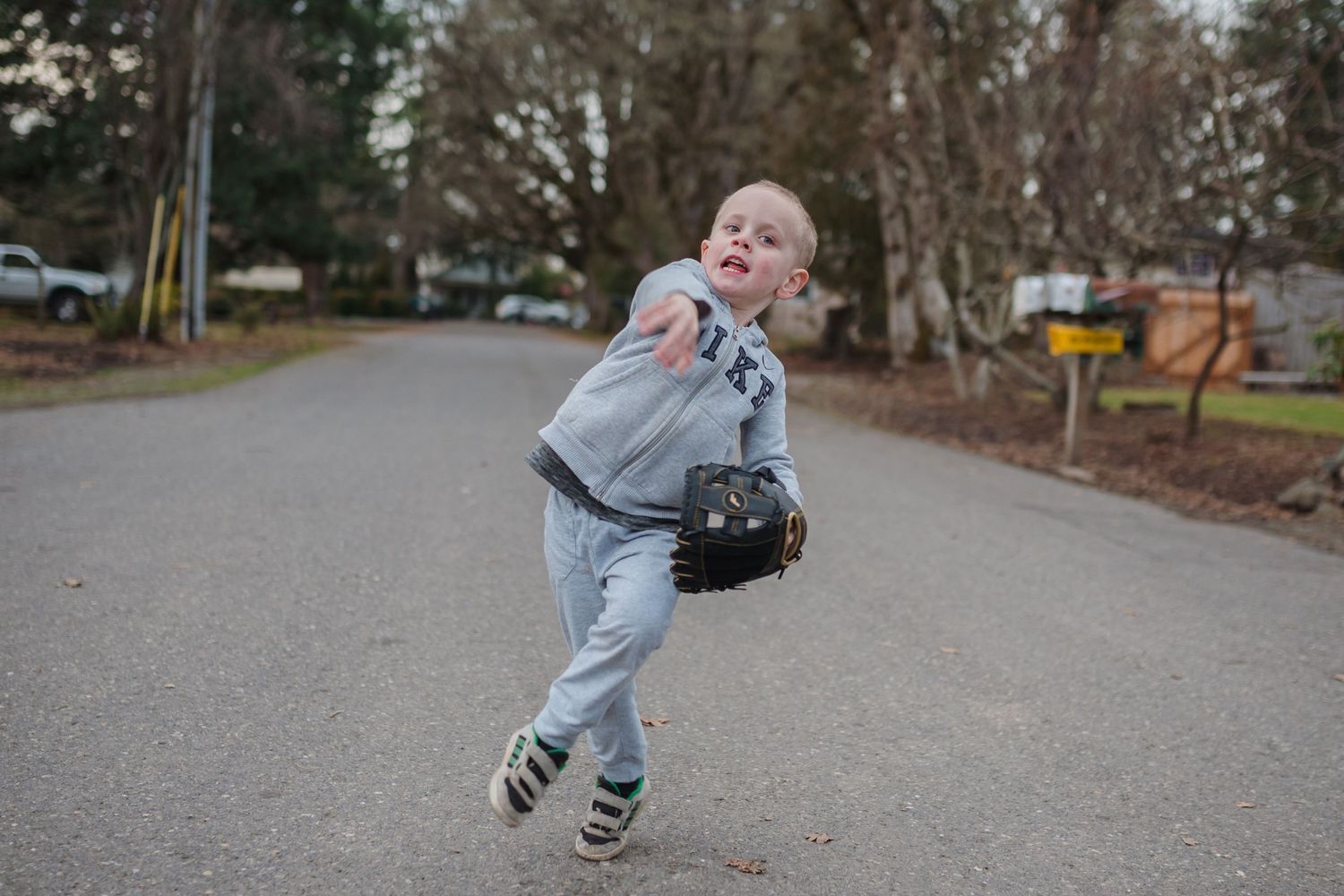 little boy throwing baseball in the middle of the street