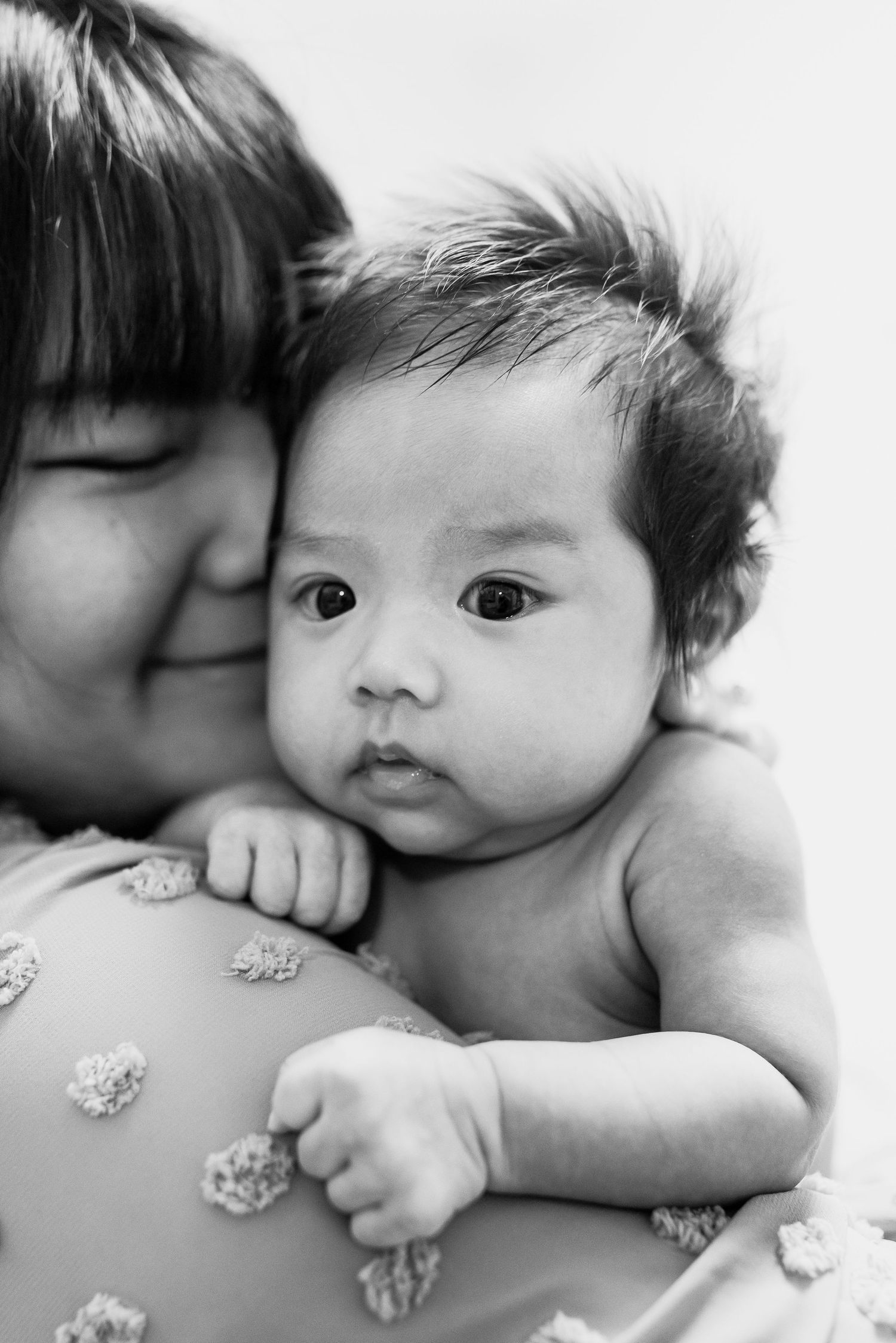 Black and white close-up series of a baby being kissed on the cheek in a tender sequence of moments.
