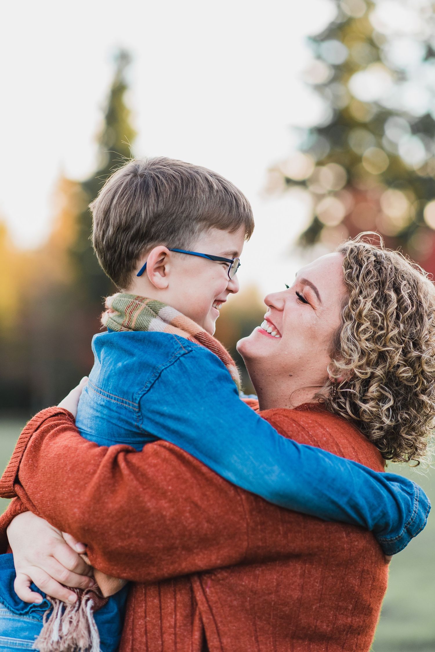 mother holding son in a hug in the air with fall color behind them