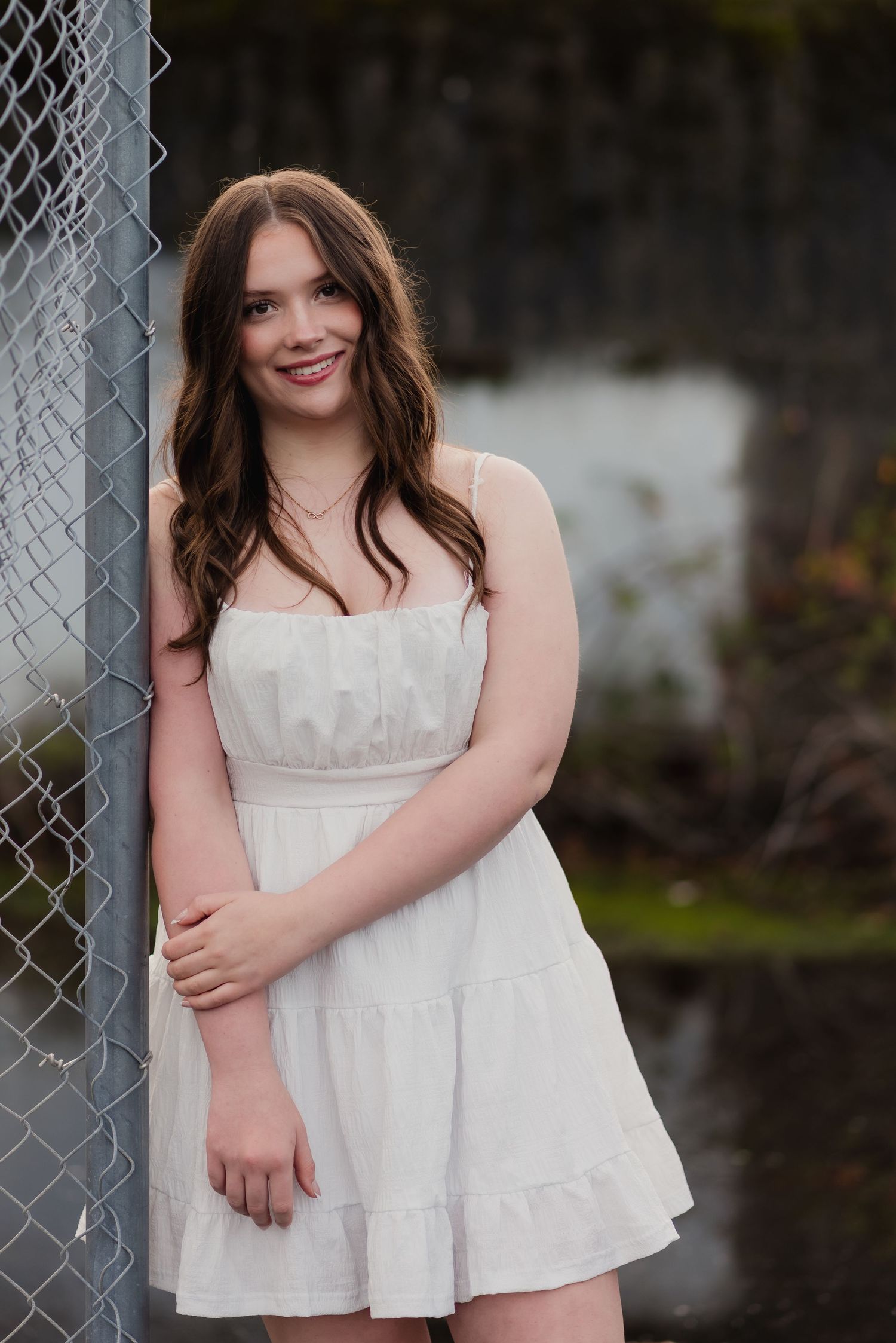 A white sundress stands out against a chain link fence and blurred natural background.