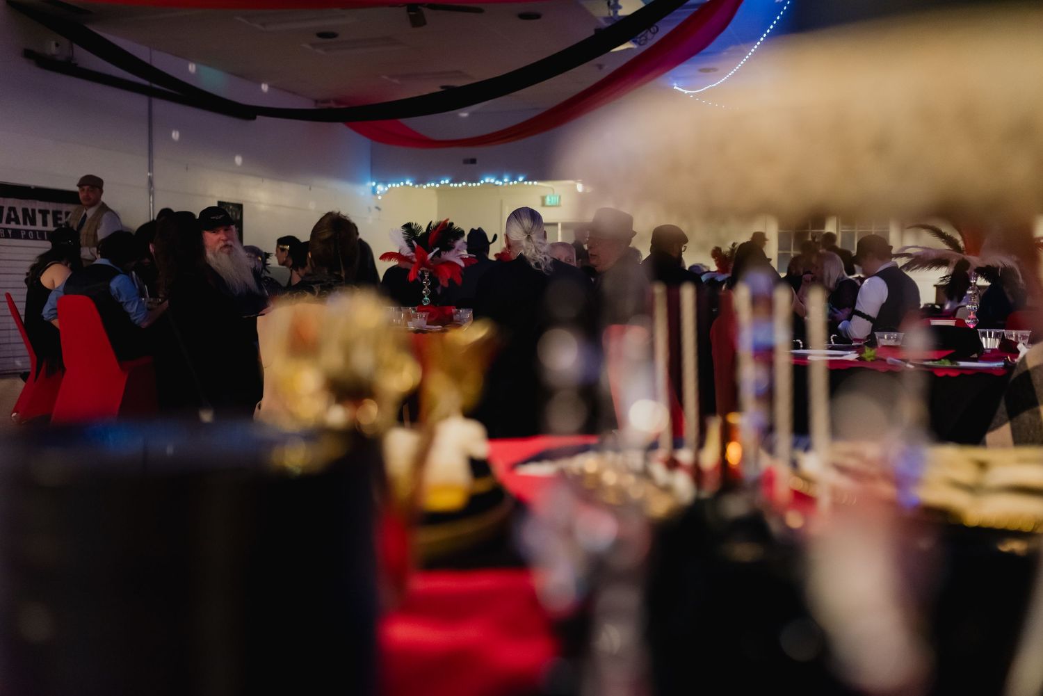 A blurred motion shot of people gathered at tables in a dimly lit event space with red and blue lighting.