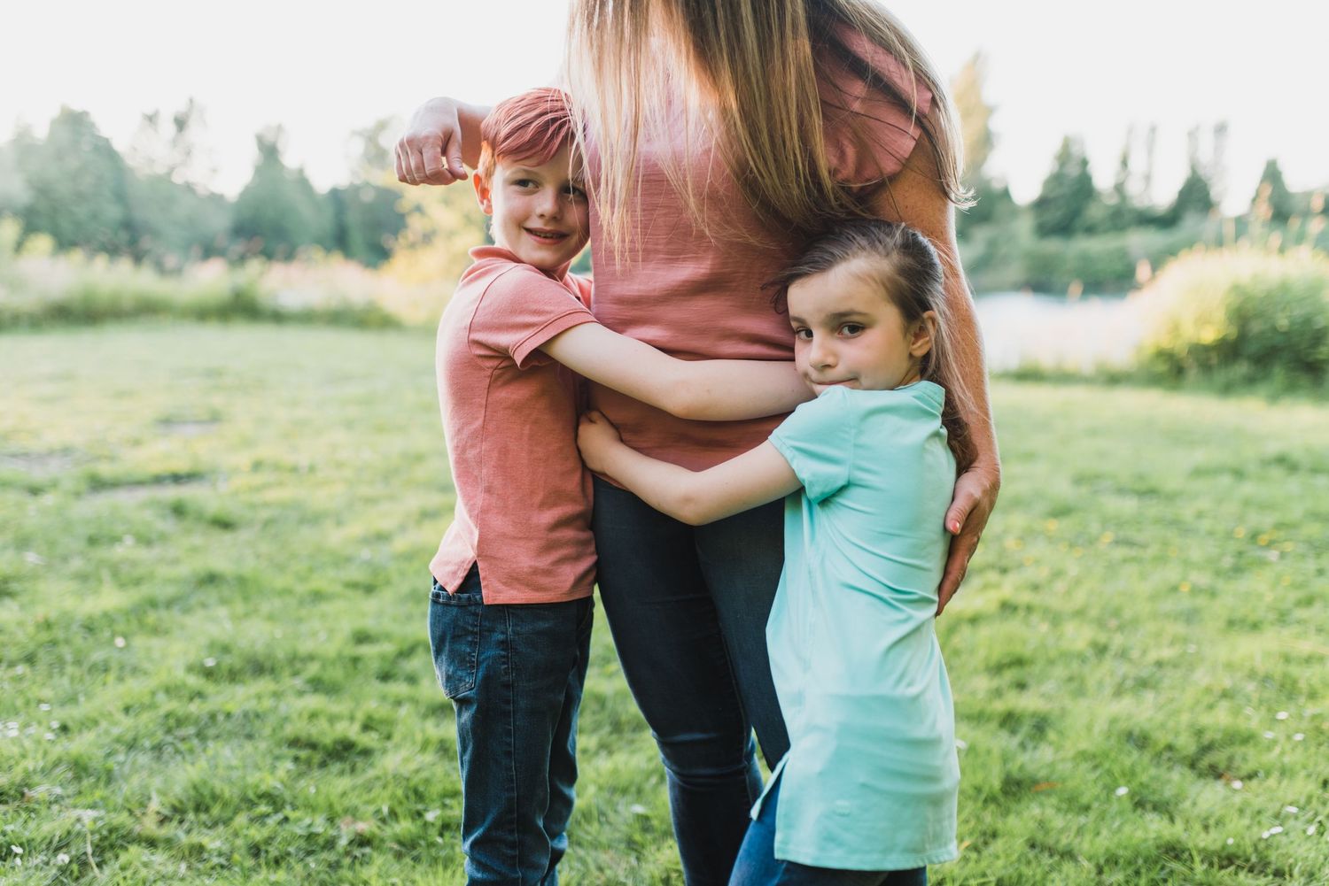 Family embracing outdoors in a grassy field during sunset.