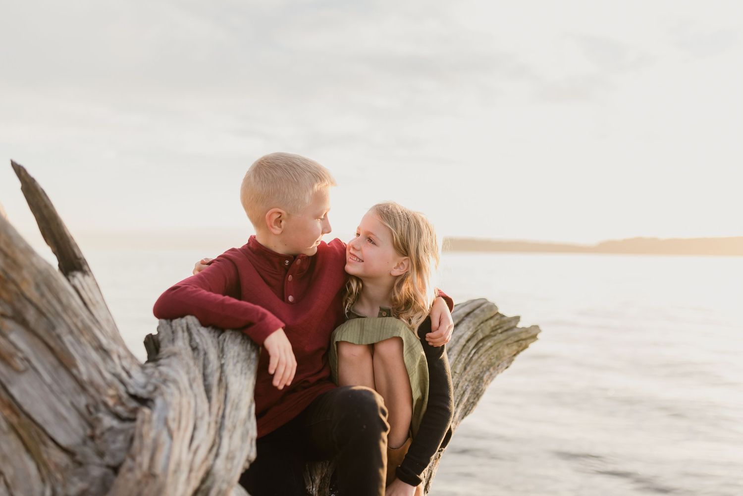 A couple shares a romantic moment on a beach at sunset with driftwood and ocean waves in the background.