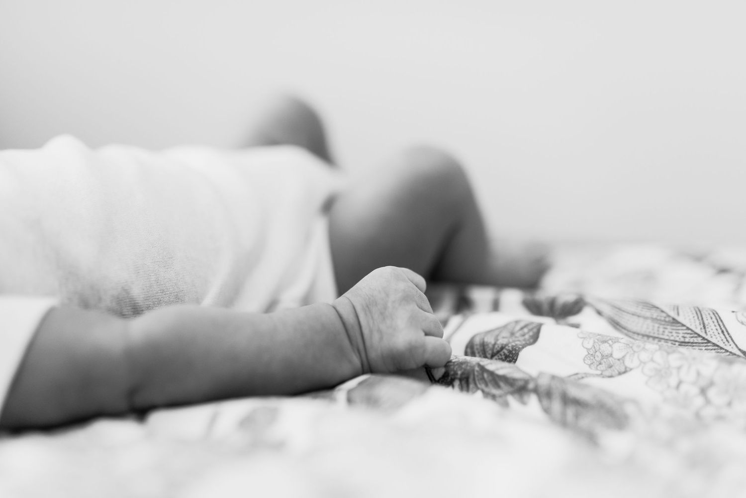 Black and white photograph of a sleeping baby swaddled in soft blankets and lying on a white bed.