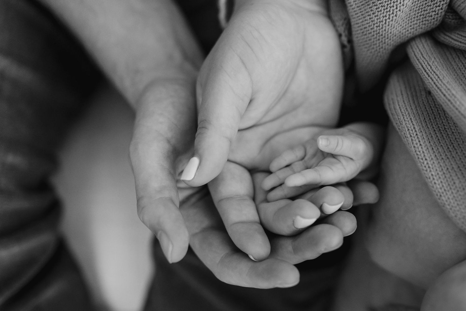 Black and white close-up sequence of tiny fingers grasping an adult's finger showing a tender moment of connection.