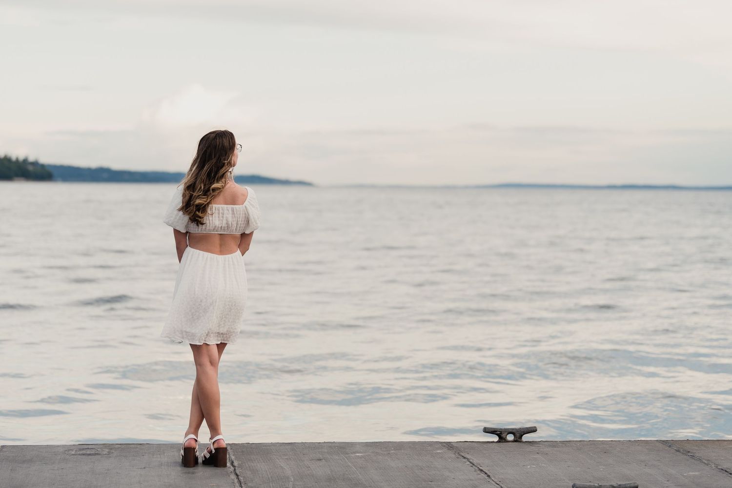 Person in white dress walking barefoot along a tranquil beach shoreline at sunset.