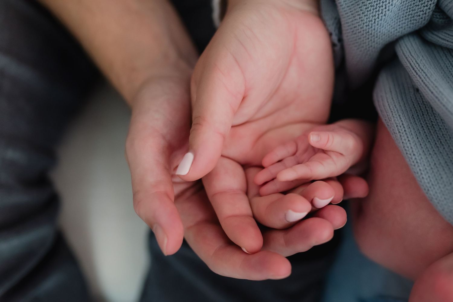 Close-up sequence of newborn baby hands grasping and moving against a gray fabric background.