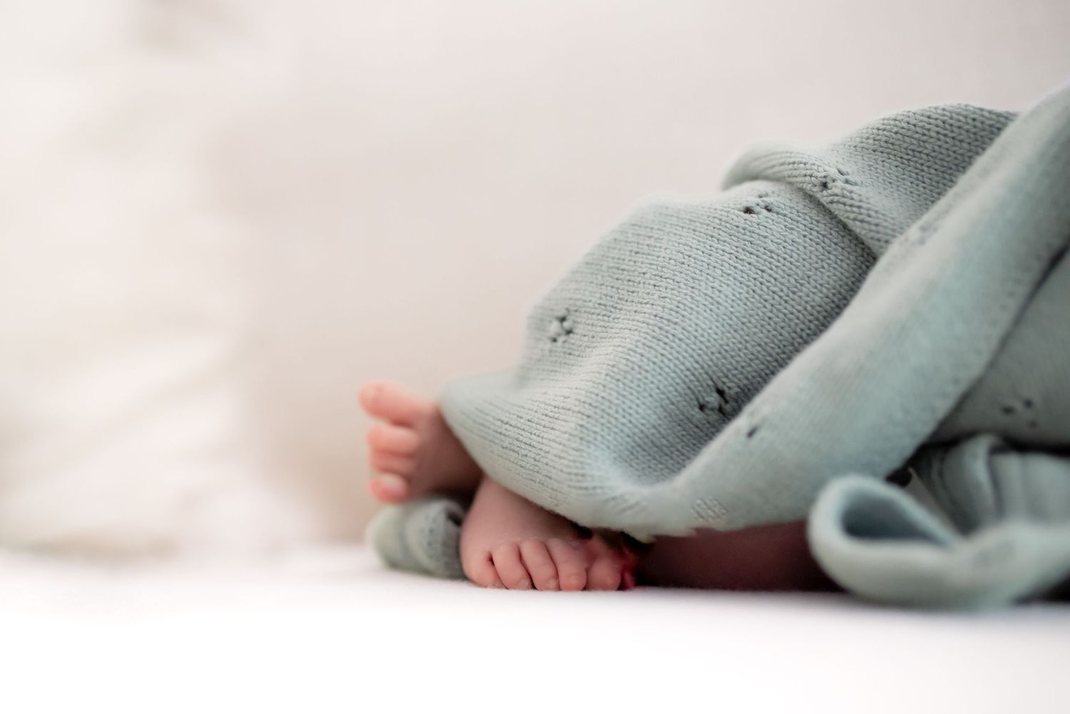 A soft mint green knitted baby blanket is draped over a newborn baby, showing tiny baby toes peeking out. Newborn photoshoot in Everett WA.