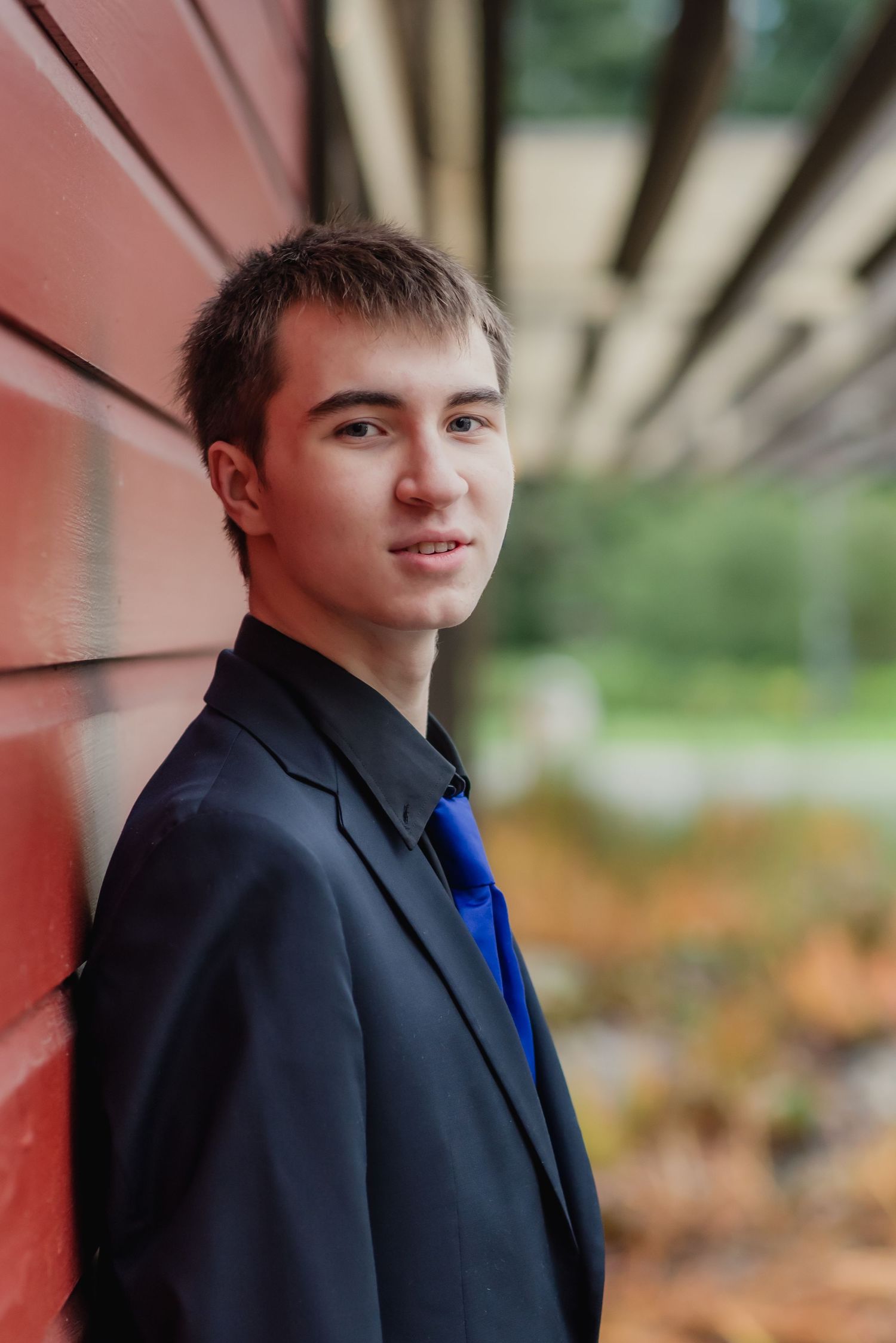 Portrait shot in black suit jacket and blue shirt against blurred outdoor background.