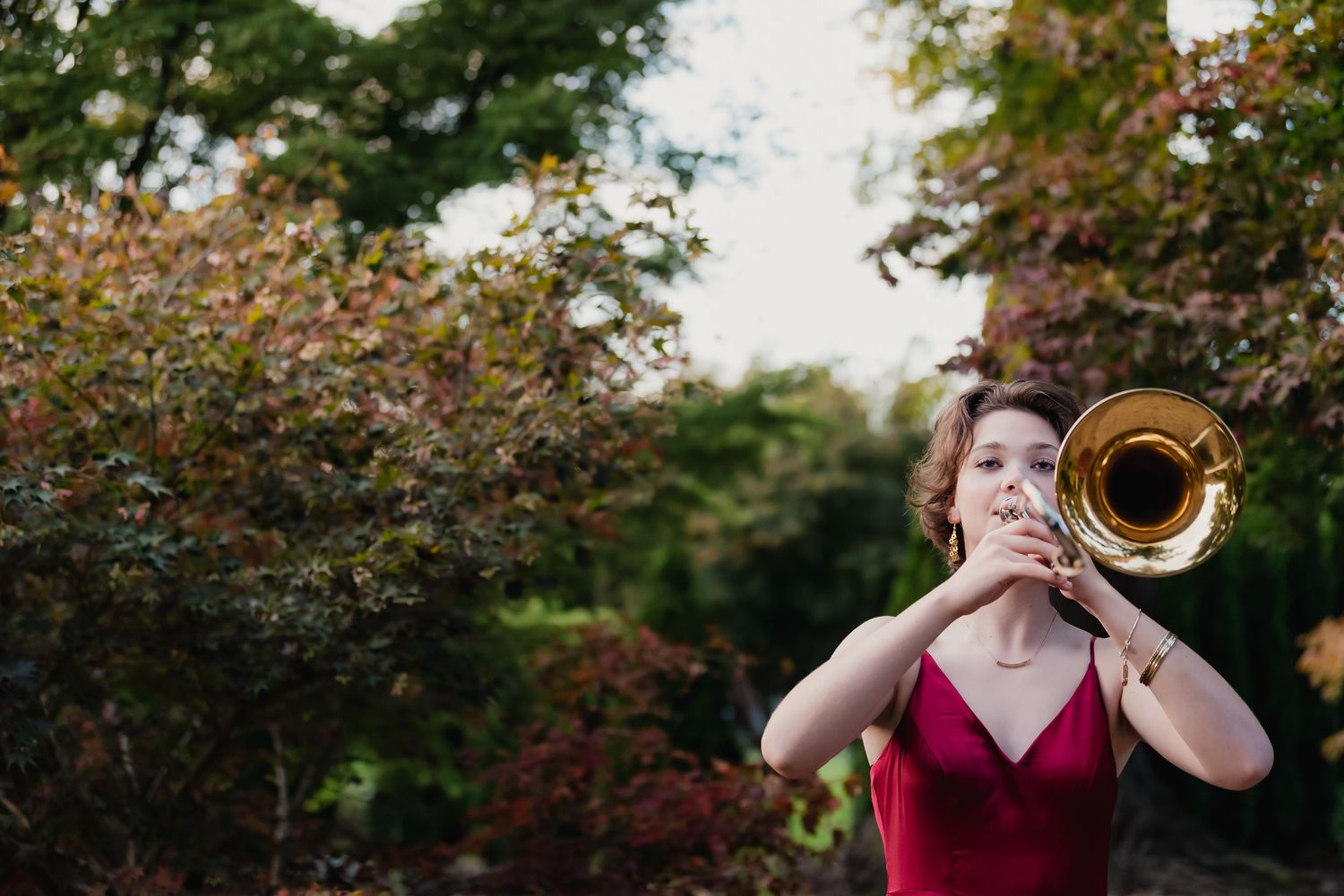 A series of photos showing a trumpet player in a red dress performing against a backdrop of autumn foliage.