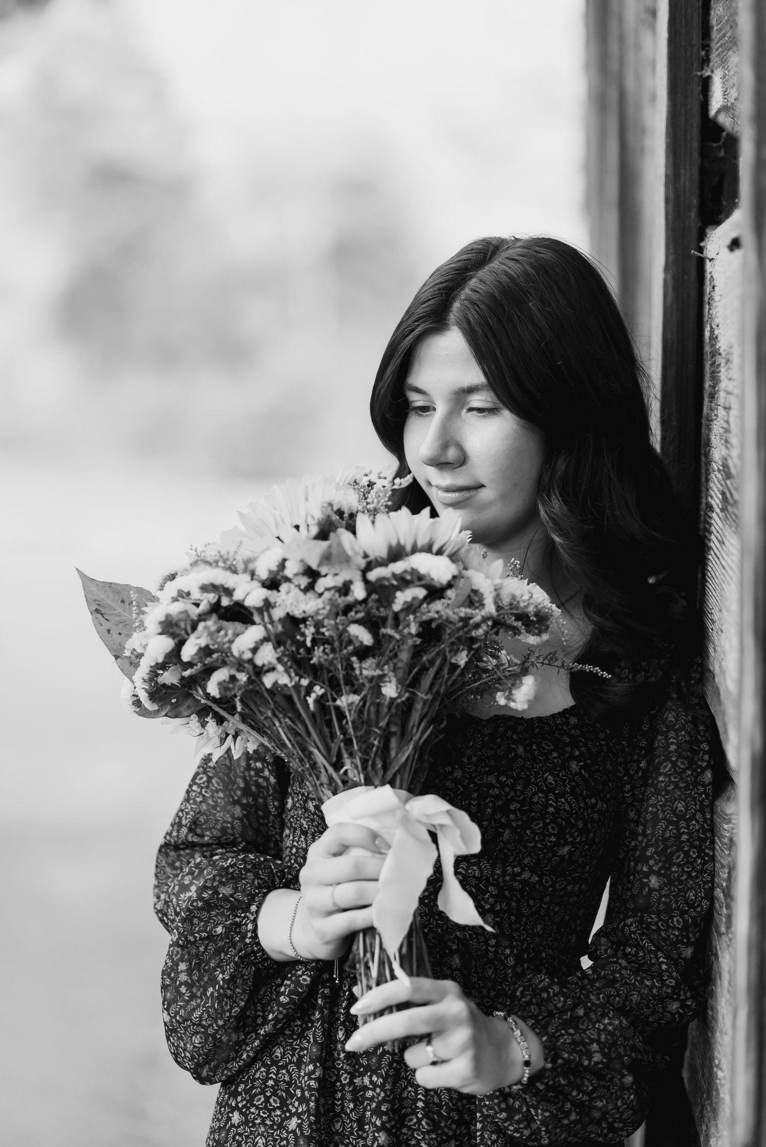 Black and white portrait of someone in a dark sweater holding a bouquet of flowers while looking down pensively.