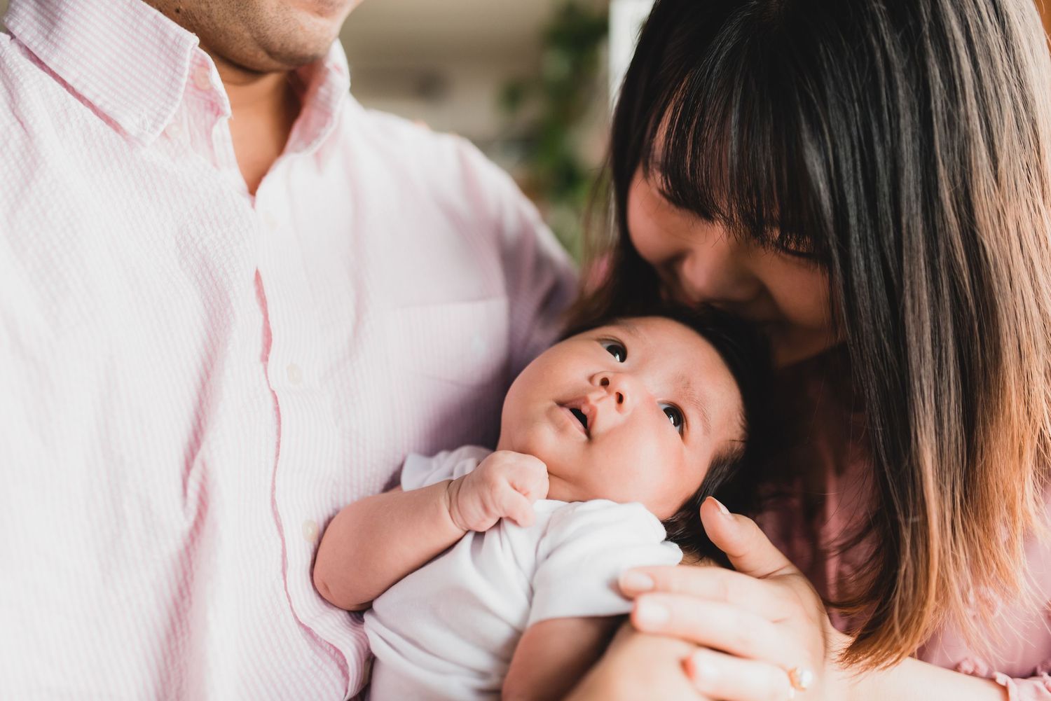 A mother and baby share a tender moment together while sitting on a couch in a bright, sunlit room.