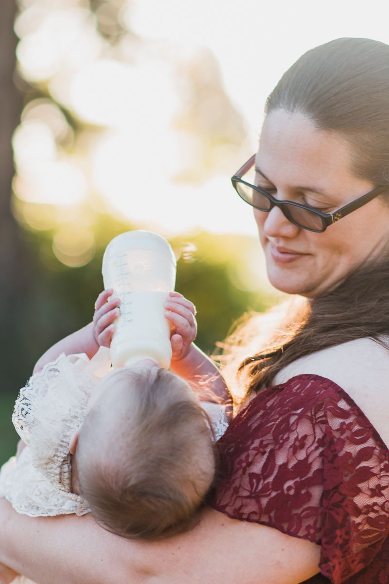 Parent in burgundy lace dress cradles baby during golden hour outdoor photoshoot.