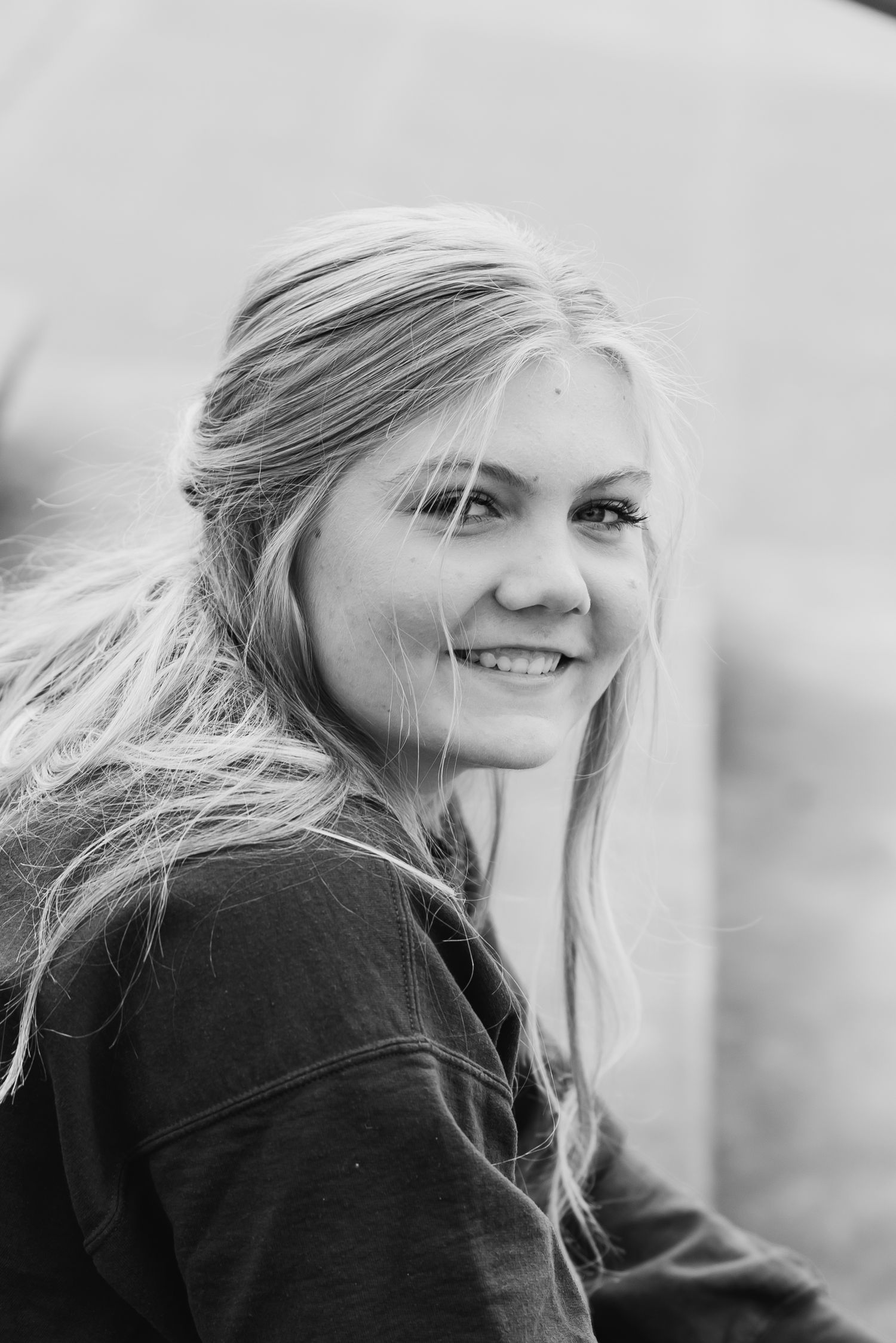 Black and white portrait of someone with windswept blonde hair smiling at the camera while wearing a dark top.
