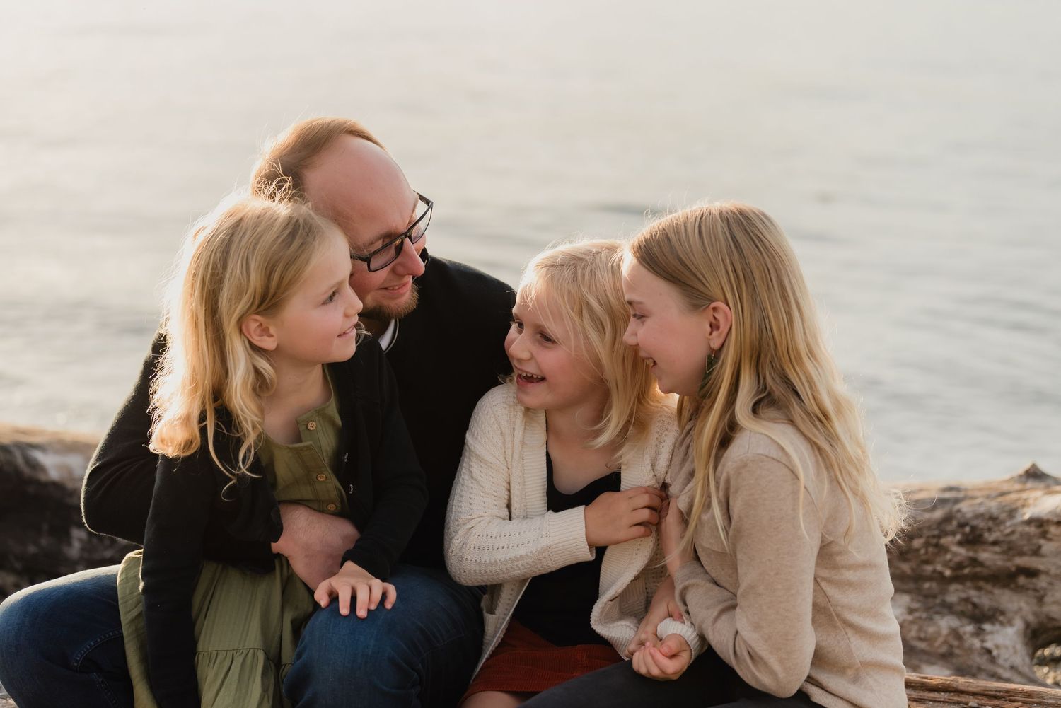 Three people share tender moments by the ocean during sunset, creating a heartfelt family portrait series.