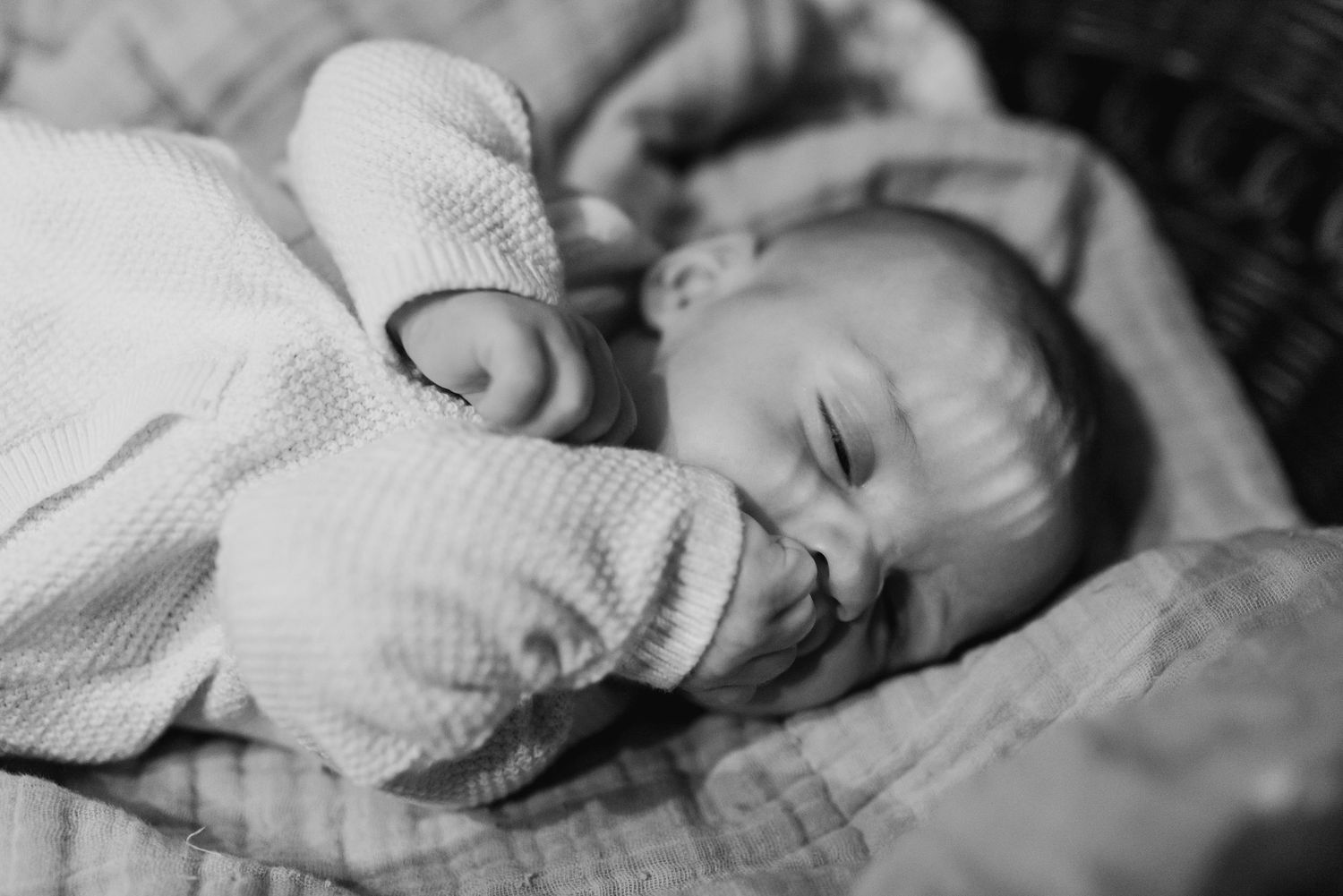 A black and white photo shows a baby sleeping peacefully in soft knit clothing.