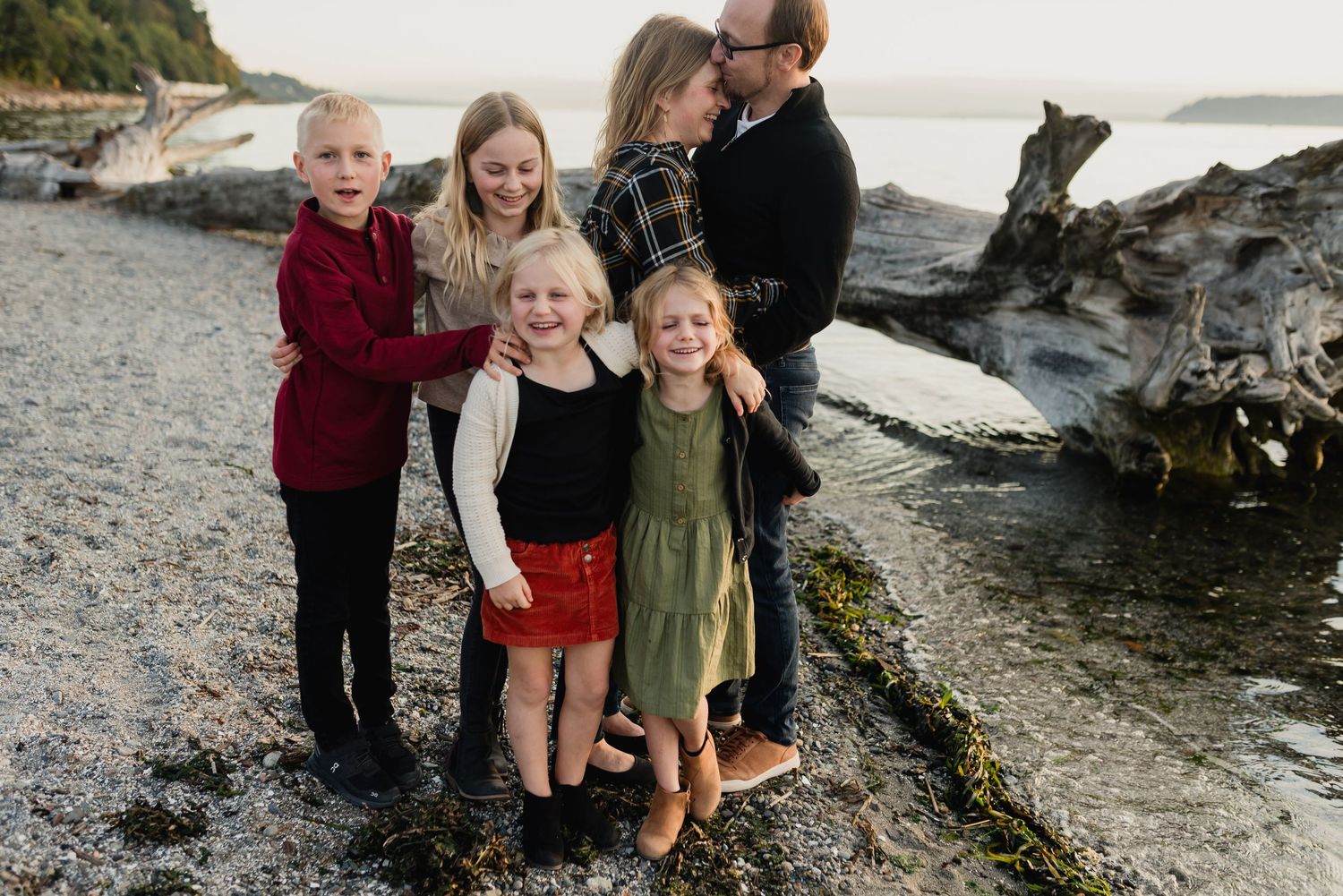 A group stands together on a rocky beach near driftwood and the ocean on an overcast day.