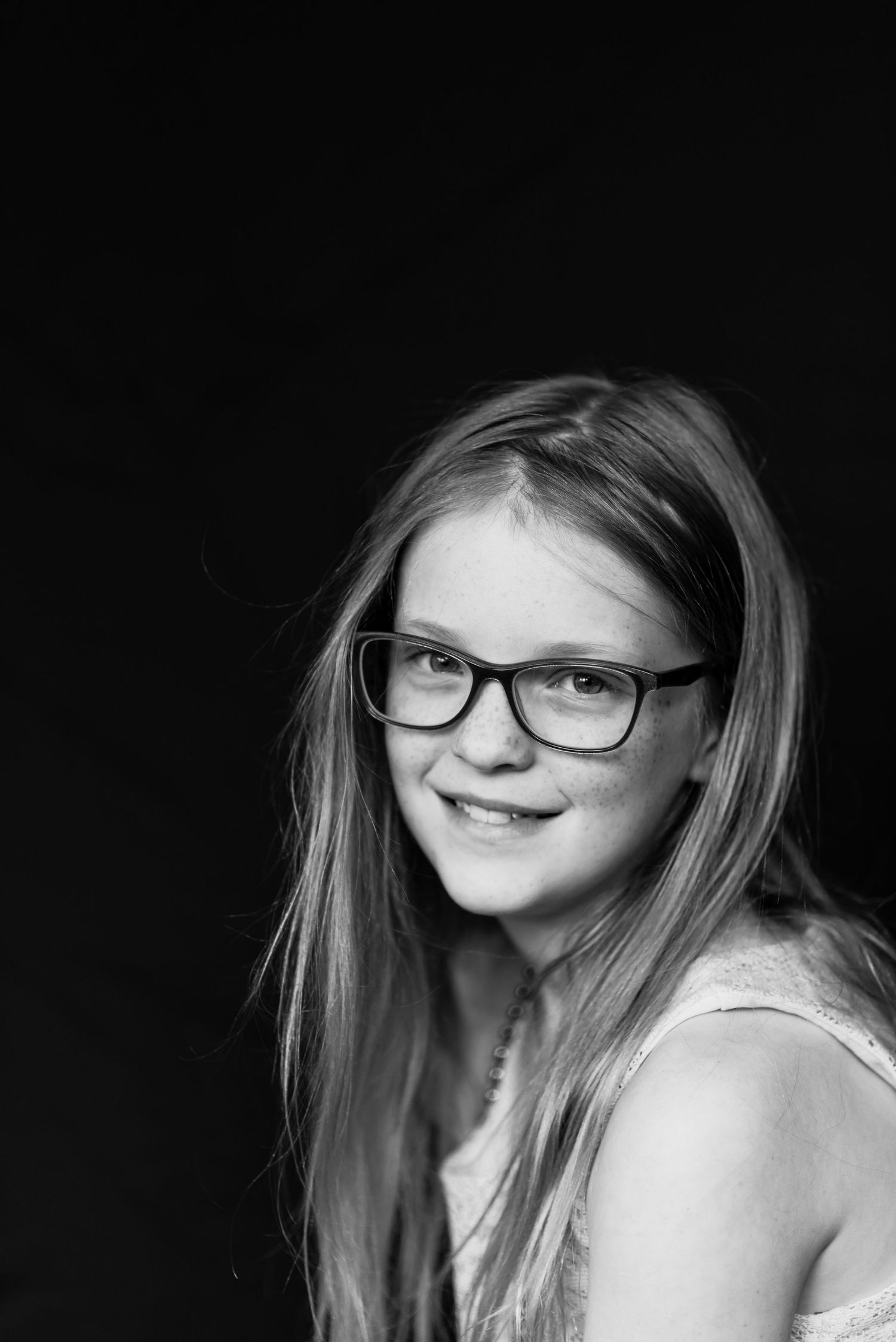black and white image of girl with glasses smiling in a portrait