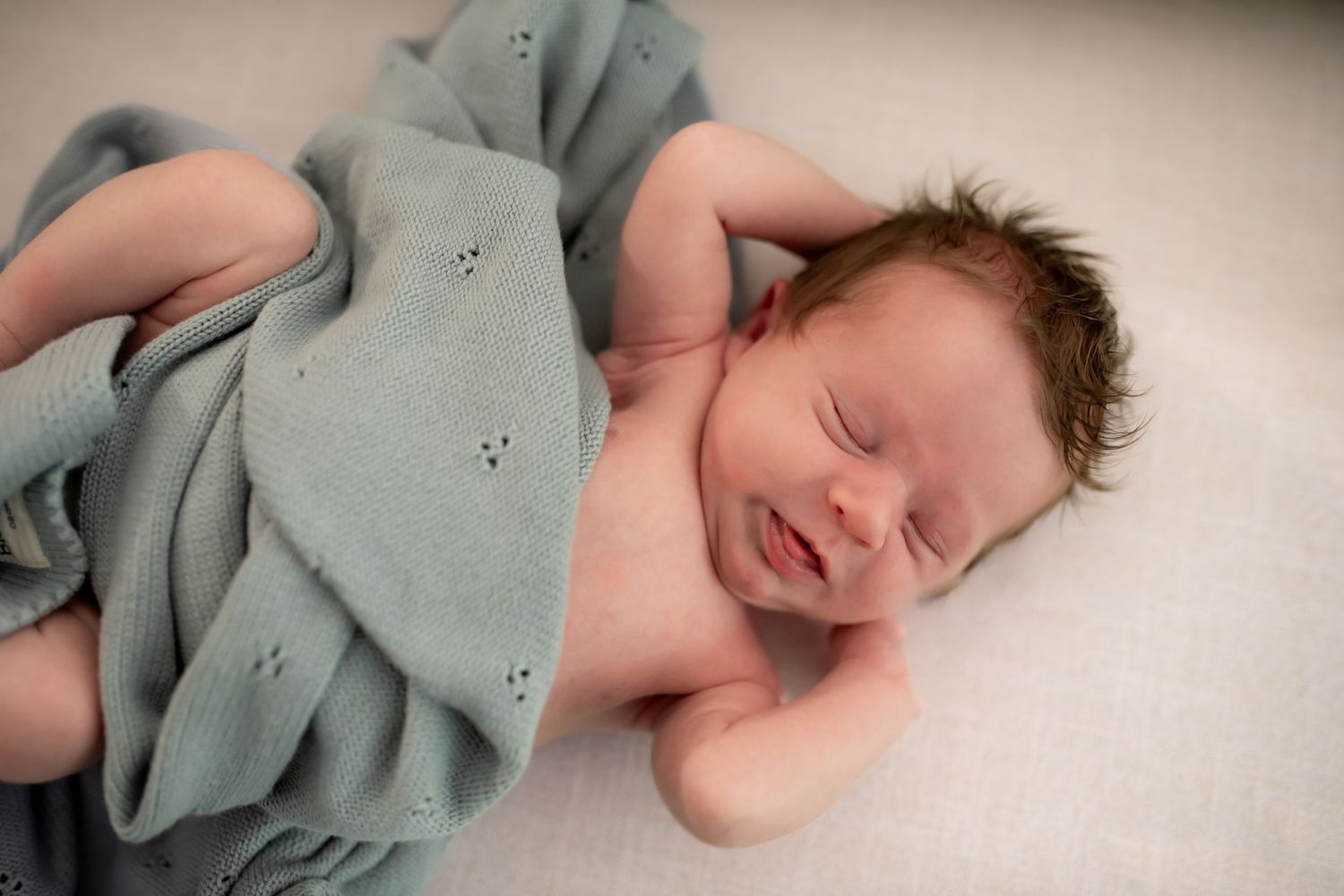 A sleeping newborn baby wearing a soft mint green blanket lies peacefully in a series of connected photos.
