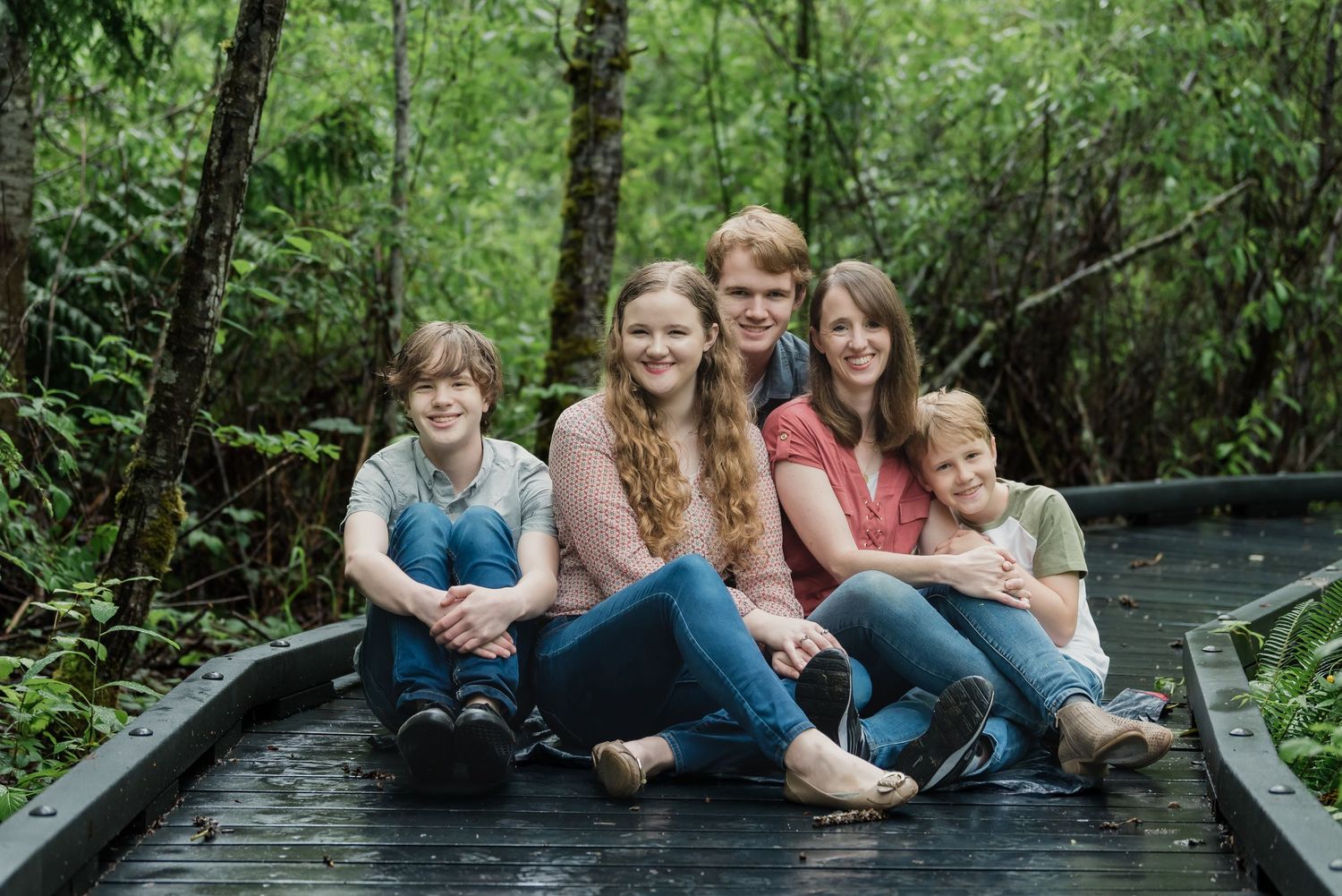 A group sits together on a wooden bridge surrounded by lush green forest and water.