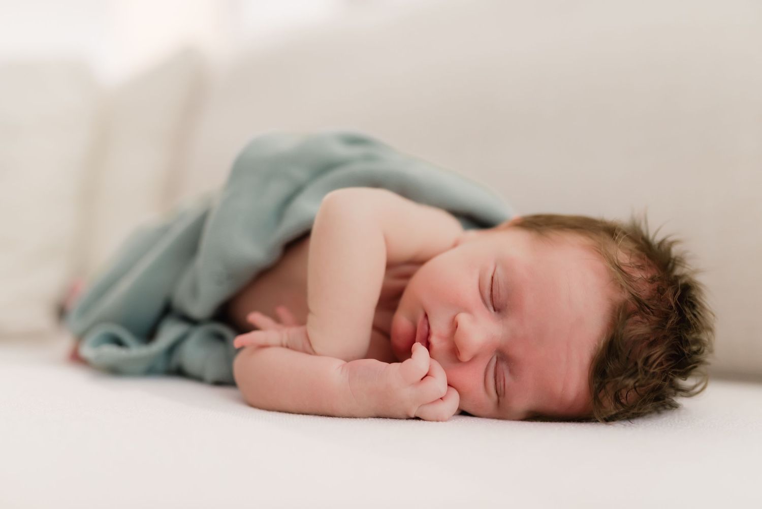 Peaceful sleeping newborn baby wrapped in soft teal blanket laying on white surface.