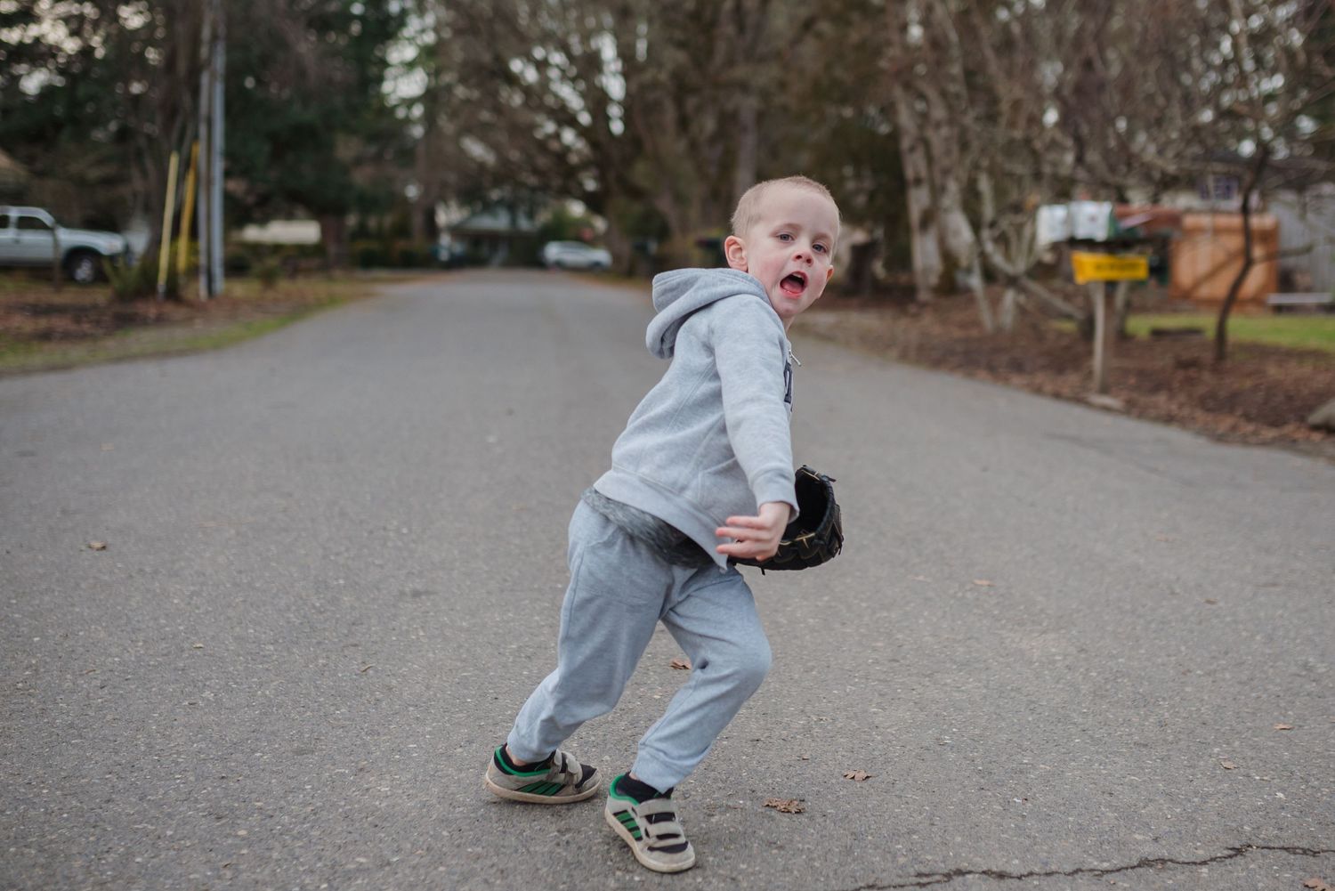 little boy throwing baseball in the middle of the street