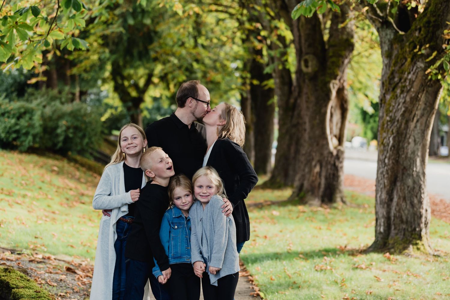 A family enjoys a playful moment together outdoors in an autumn setting with fallen leaves.
