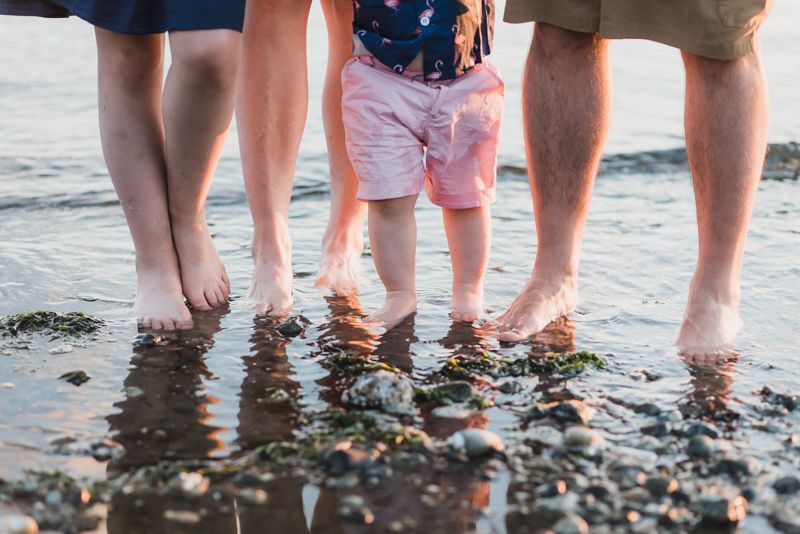 Multiple pairs of legs standing in shallow beach water during sunset creating a peaceful coastal scene.