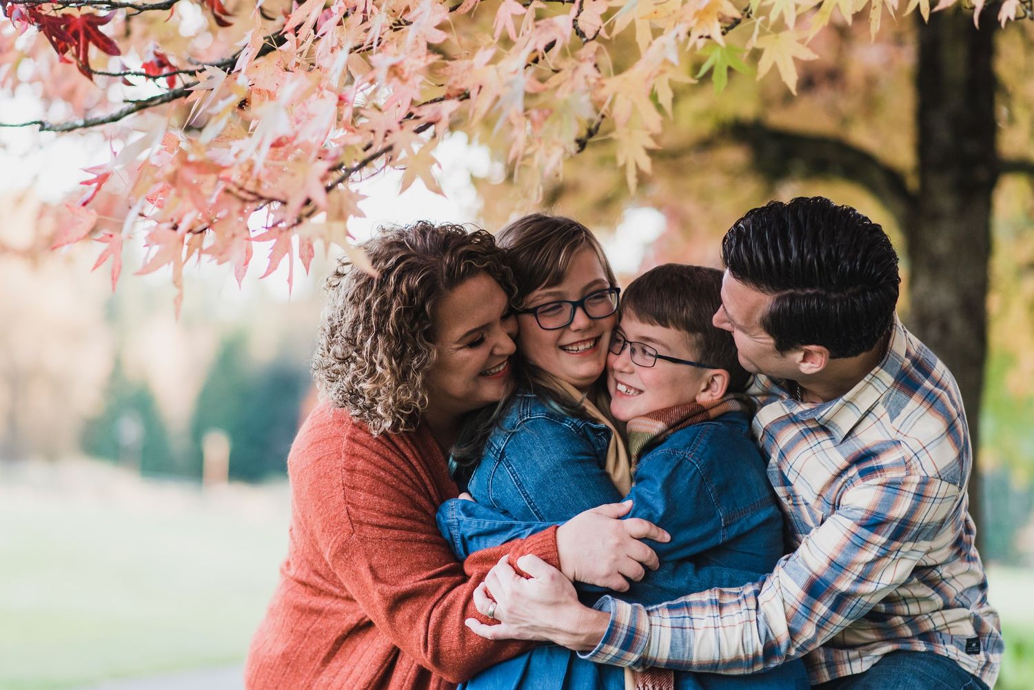 mom, dad and two kids all hugging under a tree with yellow leaves