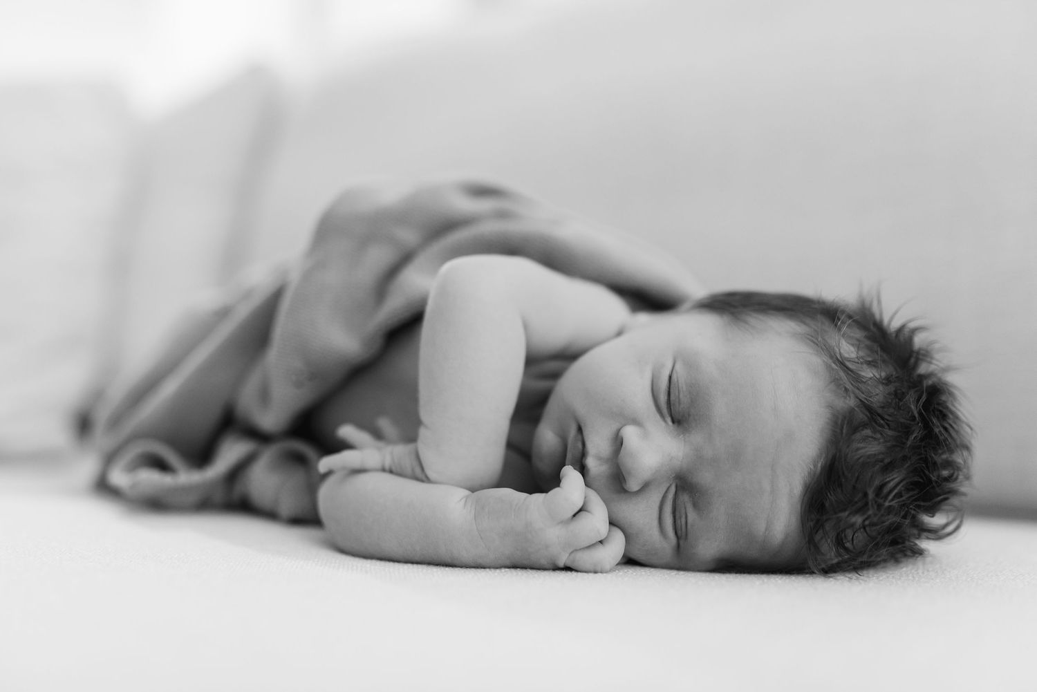 Black and white photo series showing a sleeping newborn baby in different peaceful poses against white fabric.