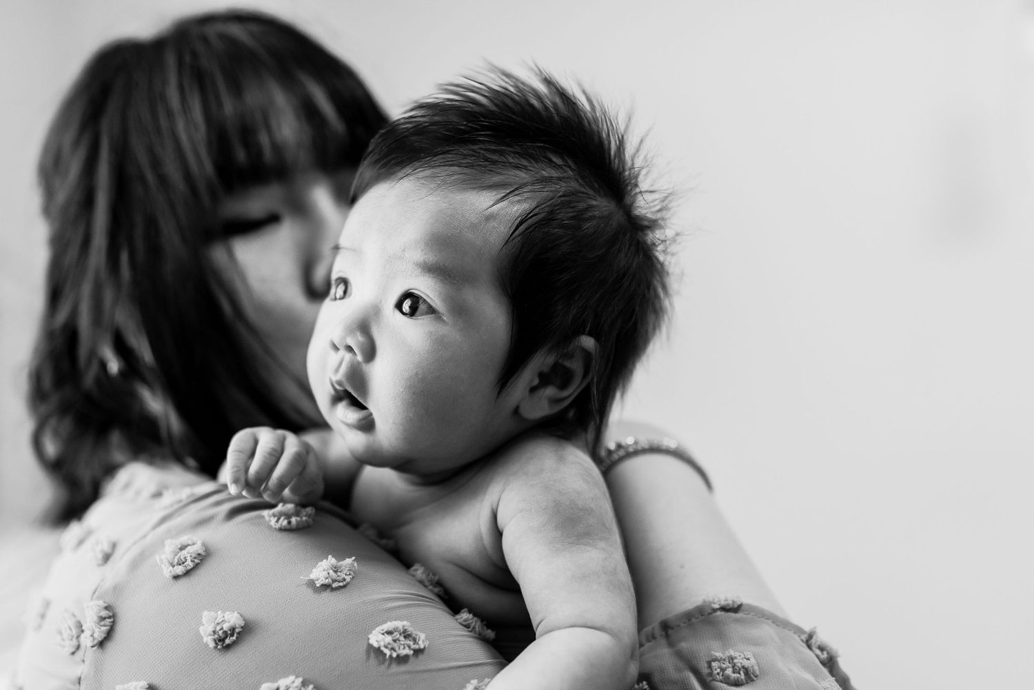 Black and white intimate portrait of a baby being held against floral fabric.