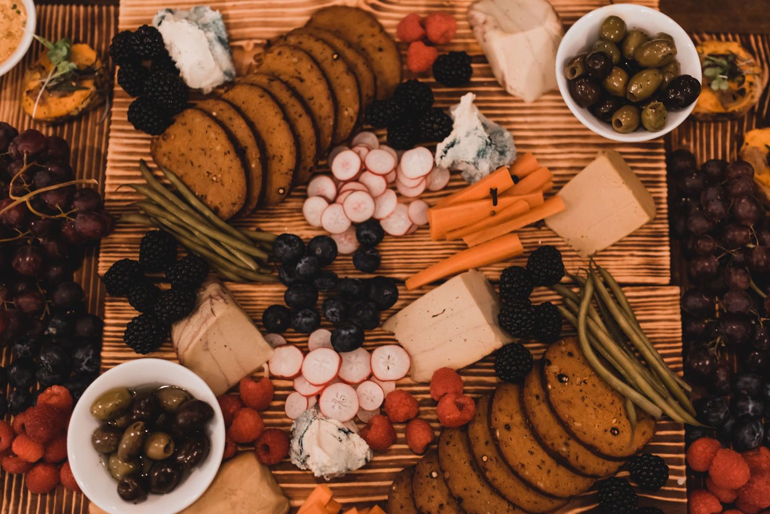 Rustic wooden table with fresh vegetables, olives, garlic, and spices arranged in a decorative pattern.
