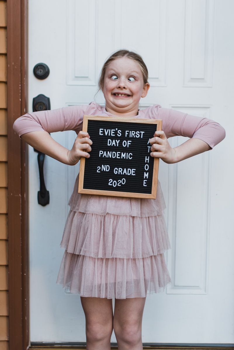 girl holding back to school sign in front of front door