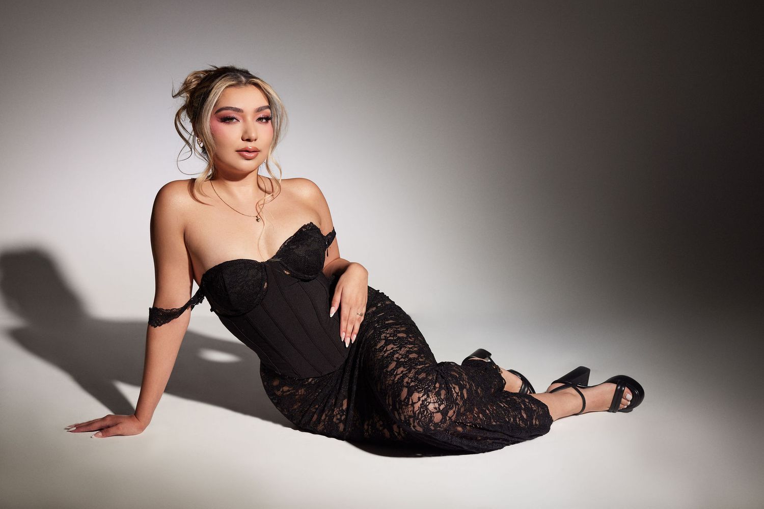 Woman in black dress posing elegantly on floor with dramatic studio lighting and shadows.