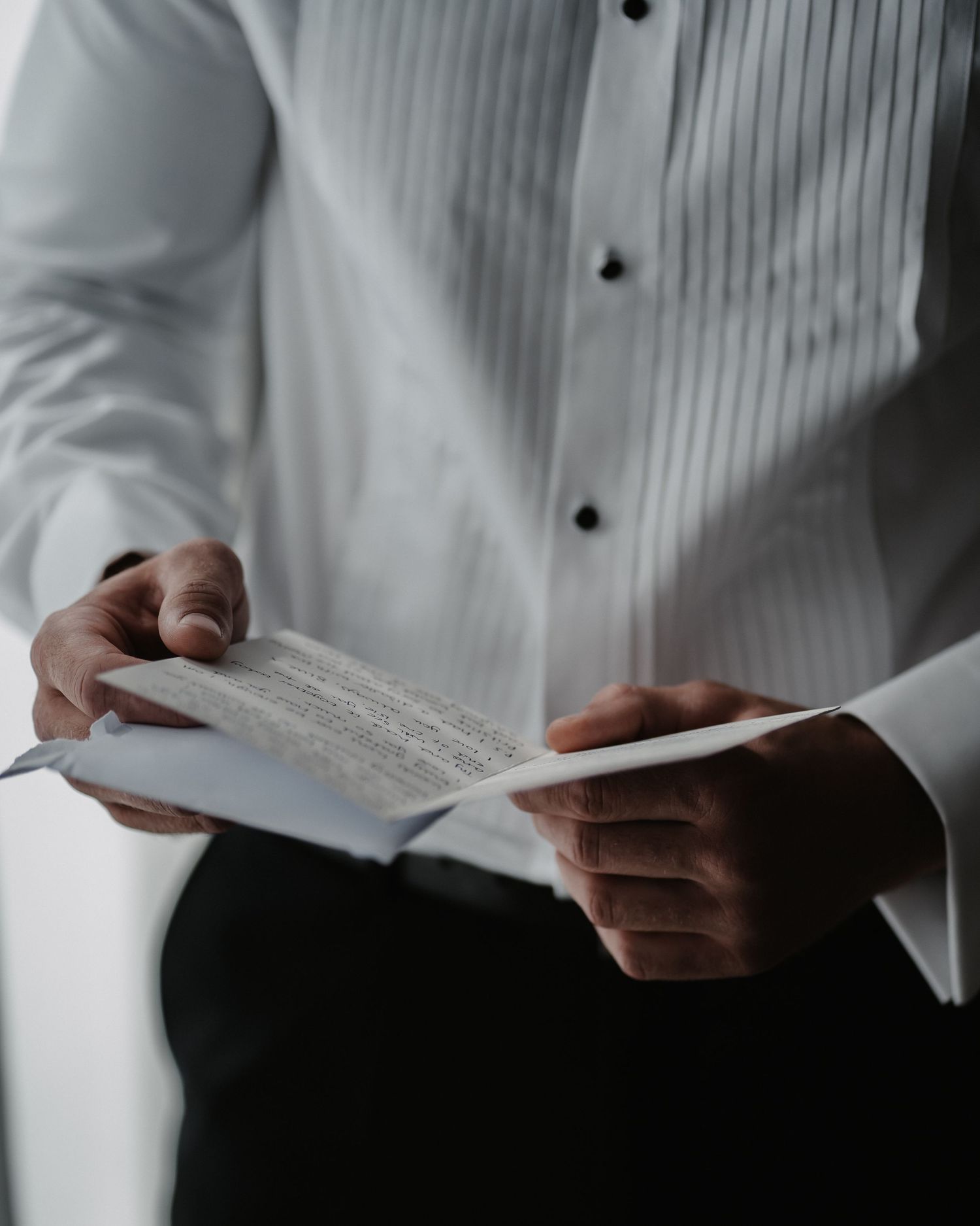 Close up detail photo of grooms hands reading the card his soon to be wife had sent him on the morning of his wedding.