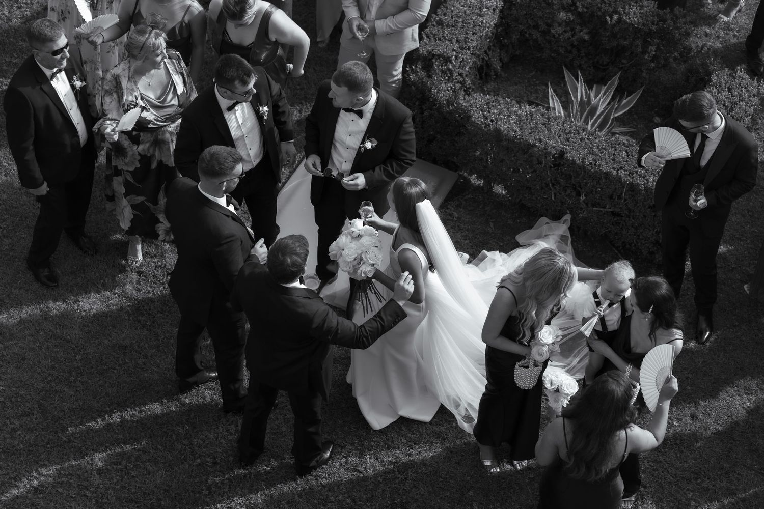 Black and white photo of the bride captured below, stood amongst all the groomsmen standing out in her white dress at he