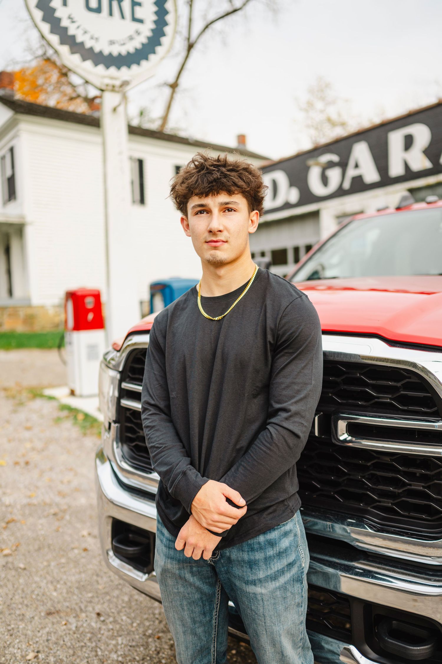 Someone in a black sweater and jeans stands in front of a red pickup truck outside a garage building.