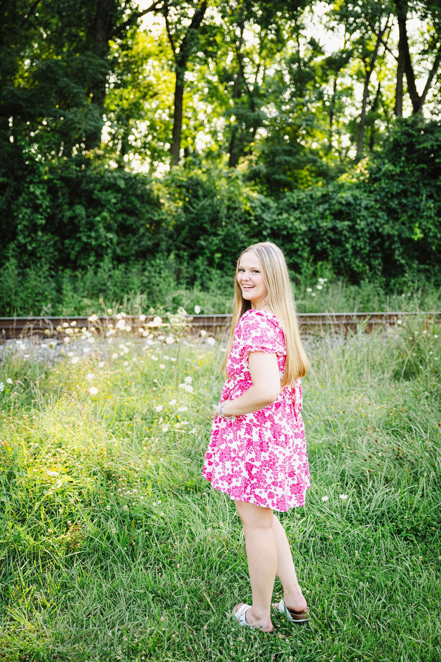 A figure in a pink floral dress twirls in a sunny meadow surrounded by tall grass and wildflowers.