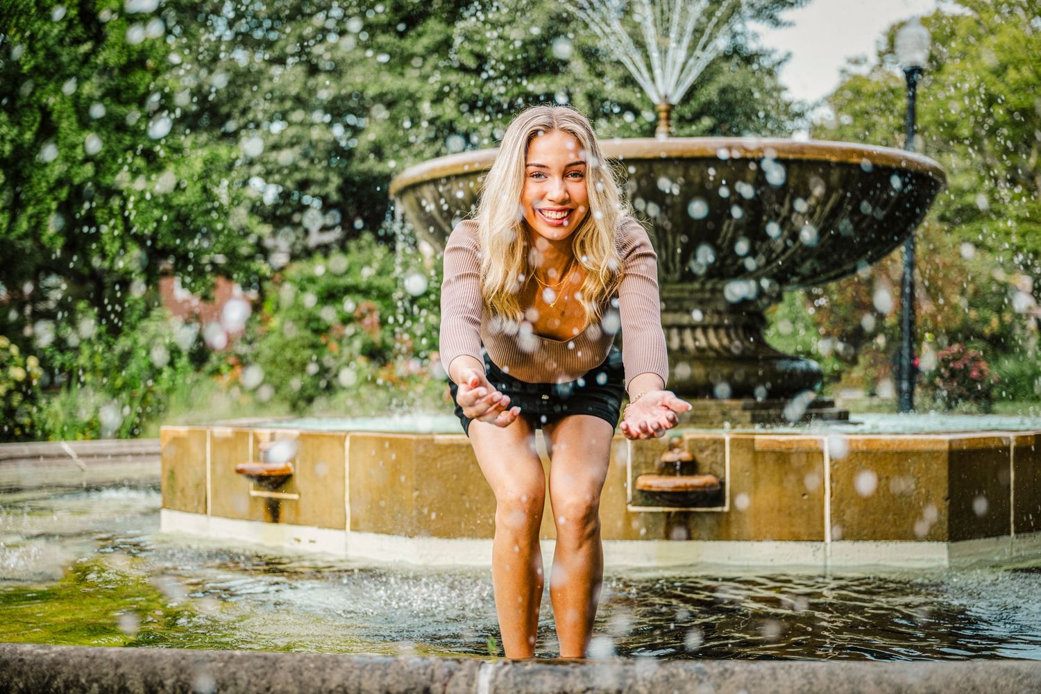 Person splashing and playing in a refreshing fountain on a sunny summer day at a park.