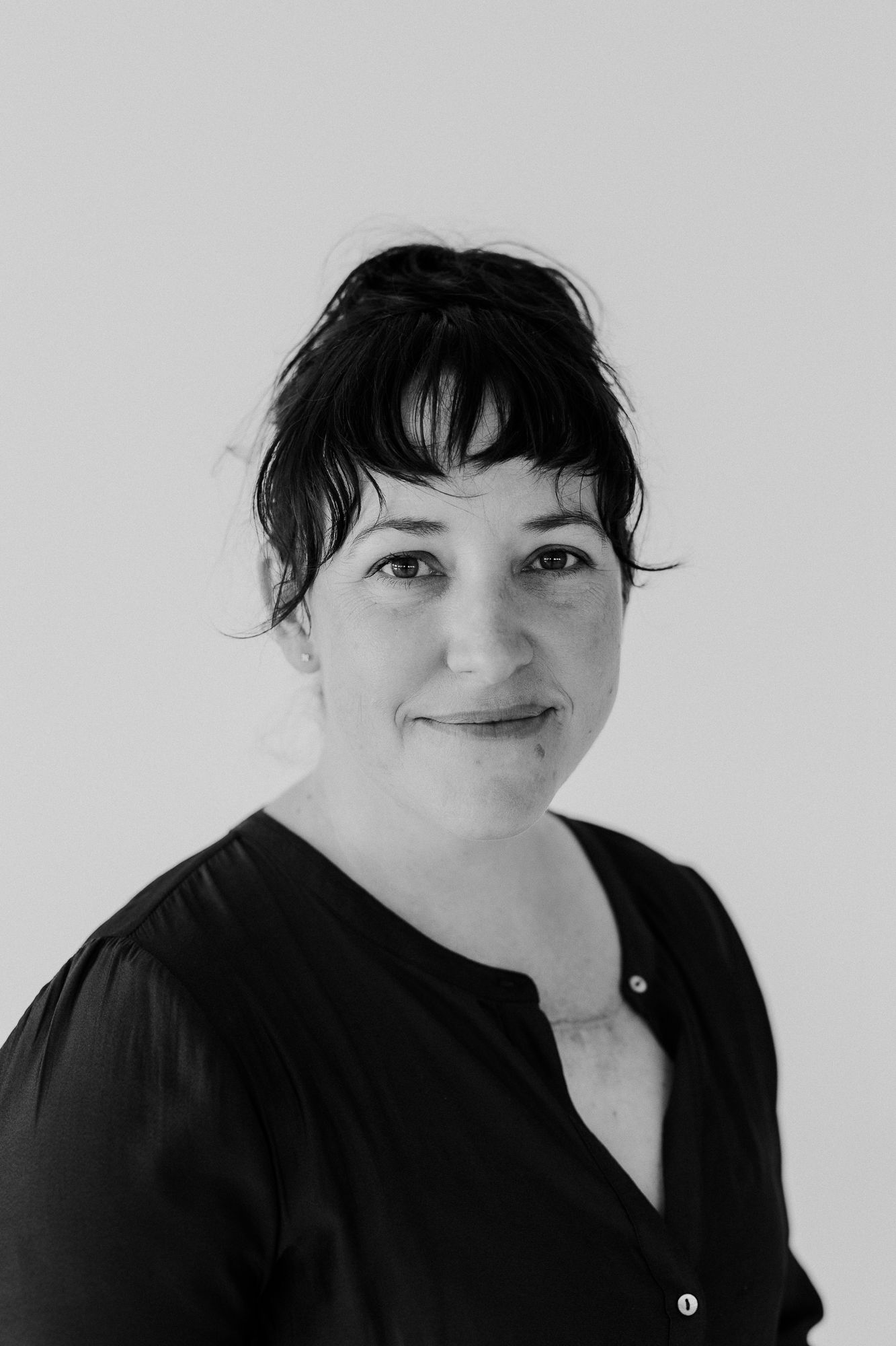 Black and white portrait of a woman with dark hair in a bun, wearing a black blouse, smiling softly.