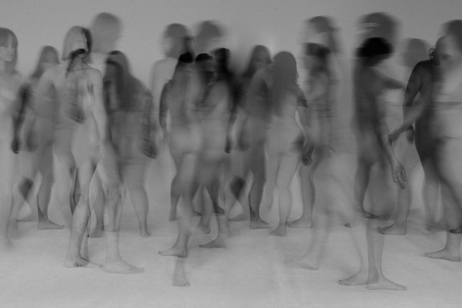Blurred black and white long exposure photo of a crowd of nude figures in motion.
