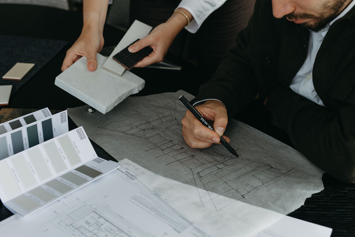 Two architects review blueprints and material samples on a table, collaborating on an interior design project.