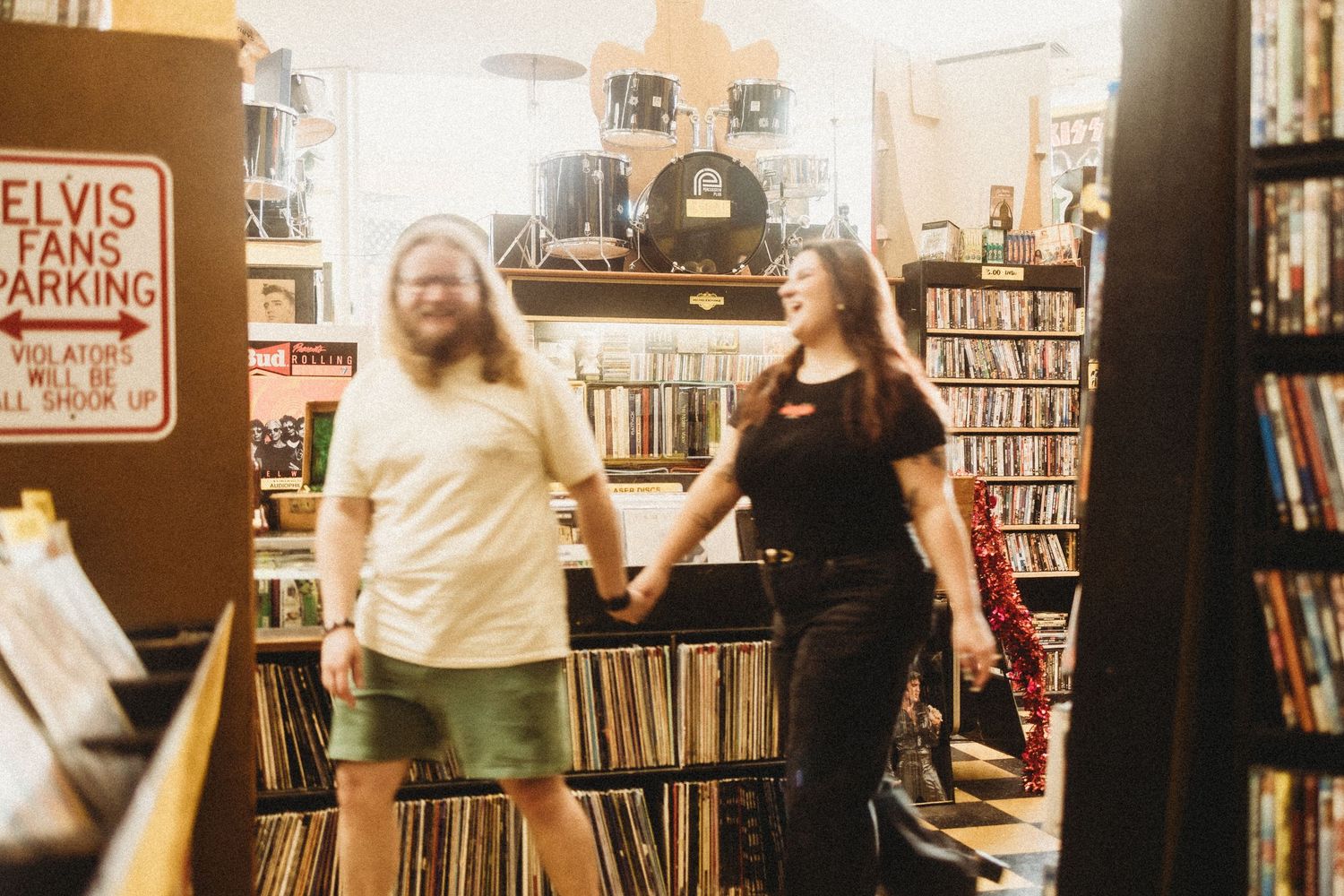 Couple holding hands and smiling in a vintage record store with Elvis Fans Parking sign. In St Louis MO