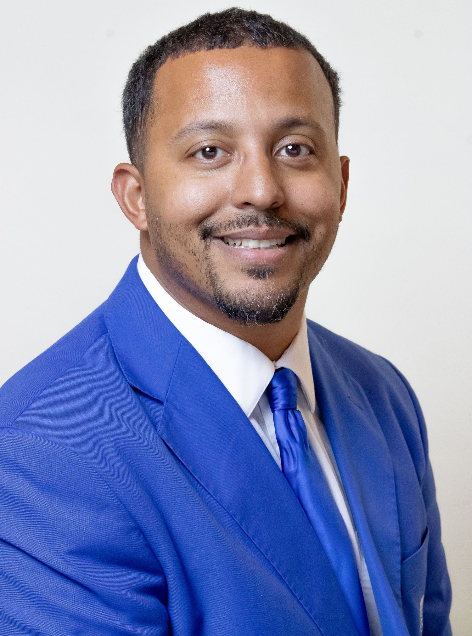 Professional man in blue suit and tie smiling confidently for a formal portrait photo.